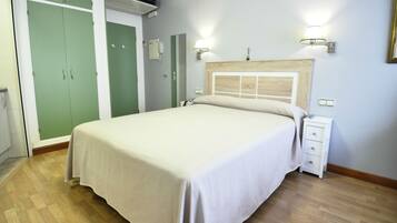 A bedroom with a bed, bedside table, nightstand, wardrobe, and a wall-mounted lamp.