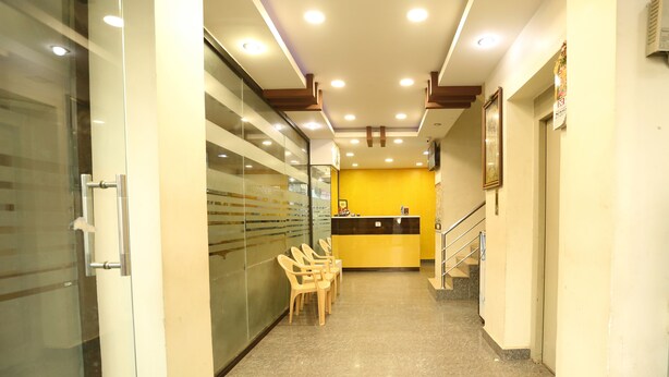A reception area with a counter, chairs, a staircase, and a glass wall. - Hotel Boopathi (Madurai)