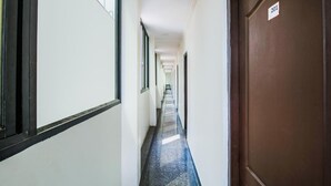 A long, narrow hallway with a blue-tiled floor and white walls. There is a door on the right with a sign that reads "201". - Hotel Boopathi (Madurai)