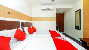 A hotel room with a bed, a ceiling fan, an air conditioning unit, and a wooden headboard. - Hotel Boopathi (Madurai)
