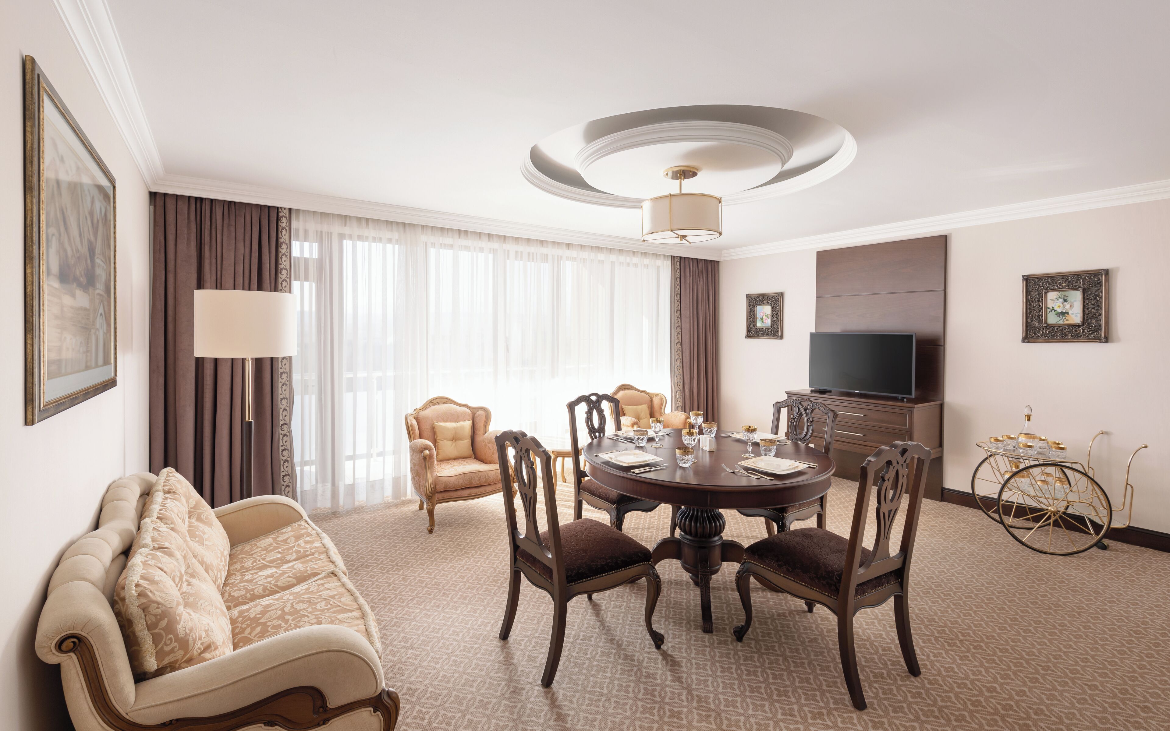 Une chambre d’hôtel comprenant une table de salle à manger ronde, quatre chaises, un canapé, un téléviseur et une lampe décorative.