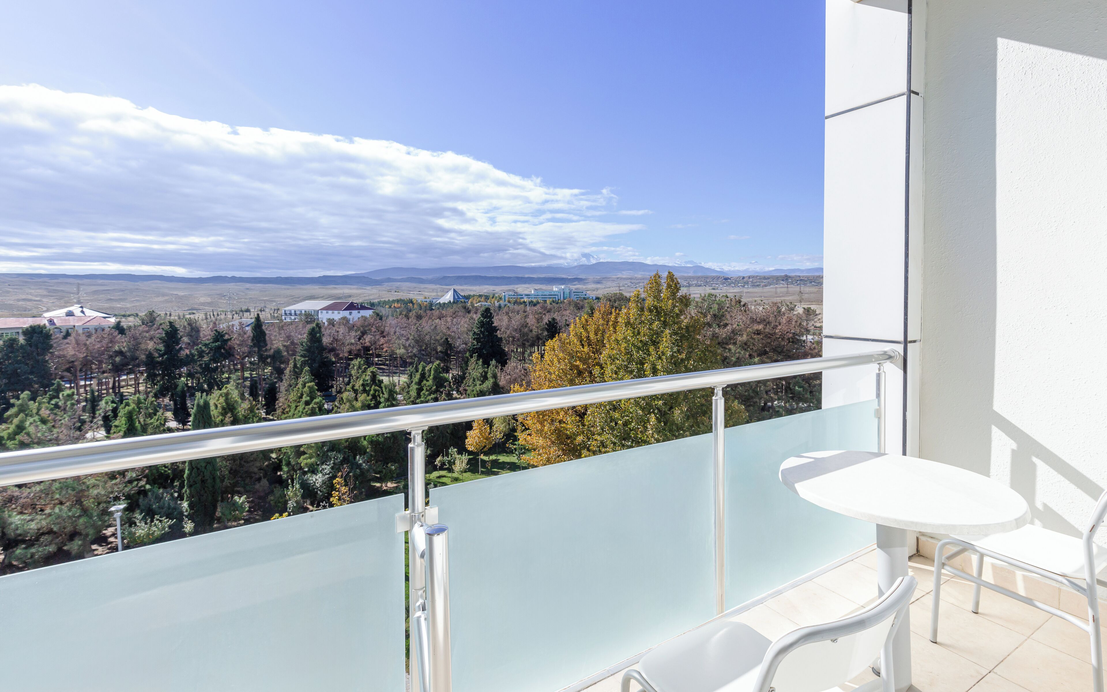Un balcón con baranda de vidrio, una mesa blanca y una silla blanca.
