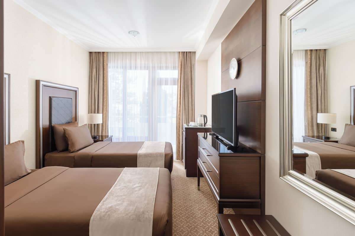 Quarto de hotel com duas camas, televisão, penteadeira e um espelho grande.