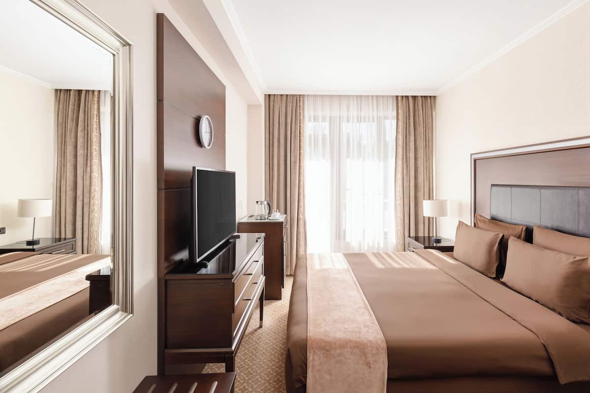 Quarto de hotel com cama grande, televisão, cómoda e espelho.