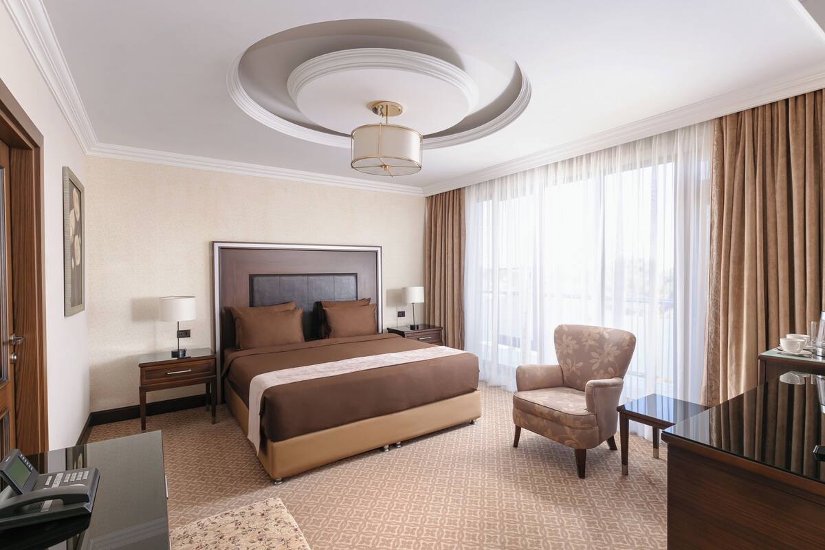 Quarto de hotel com uma cama grande, uma cadeira, uma escrivaninha e uma televisão.