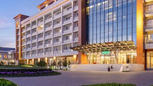 A multi-story hotel with a modern facade, a covered entrance, and a landscaped area with purple flowers. - Chinar Health Hotel Naftalan (Naftalan)