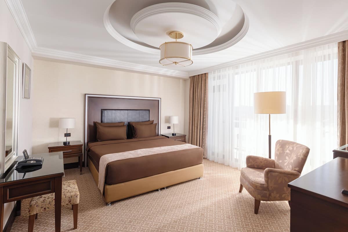 Quarto de hotel com uma cama grande, uma escrivaninha com cadeira, televisão e luminária.