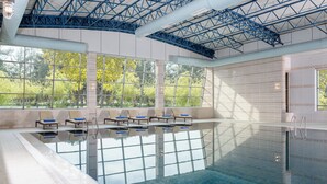 Une piscine avec des parois en verre transparent, des chaises longues et une vue sur les arbres à travers de grandes fenêtres.