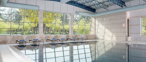 Une piscine avec des parois en verre transparent, des chaises longues et une vue sur les arbres à travers de grandes fenêtres.