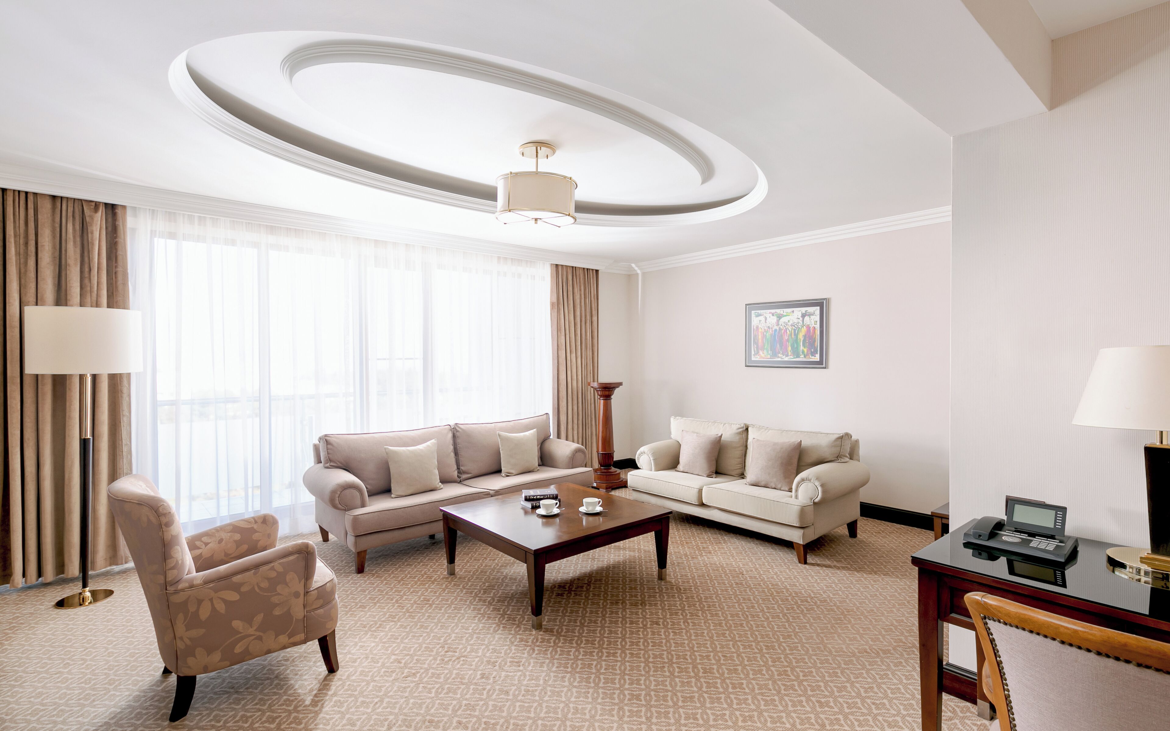 A well-lit living room with two sofas, a coffee table, and a desk with a phone.