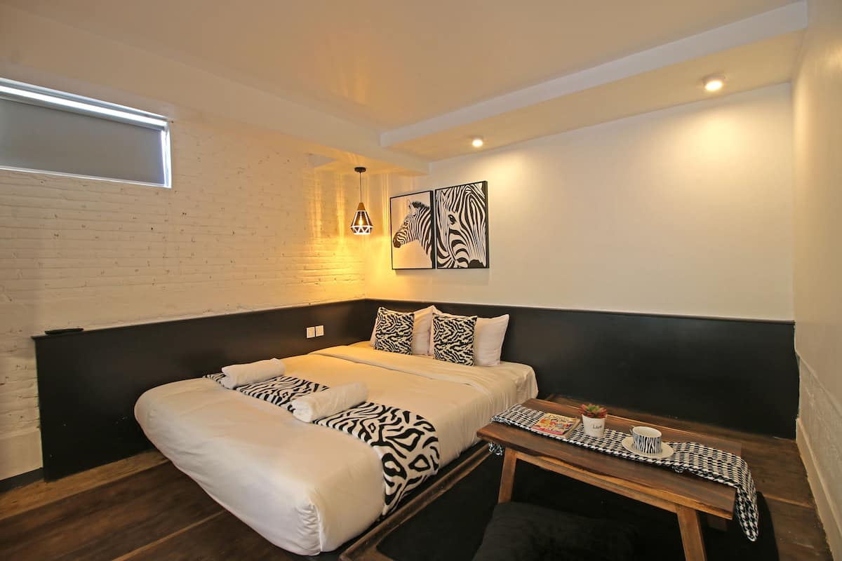 A modern hotel room with a large bed, a small table, a zebra-themed artwork, and a brick wall.