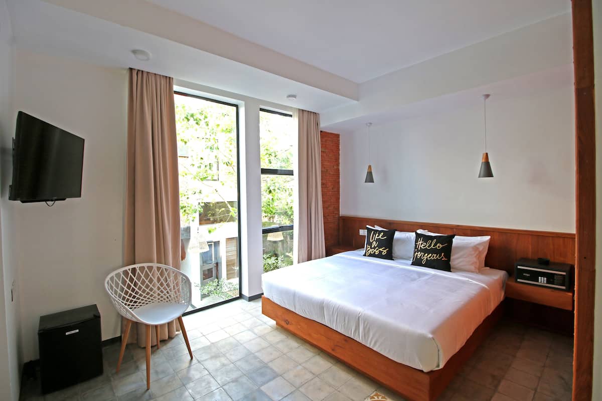 A bedroom with a bed, a chair, a TV, and a window with curtains.