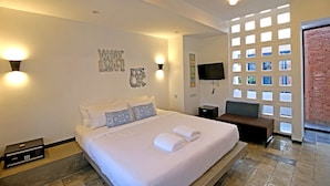 A hotel room with a large bed, a flat-screen TV, a seating area, and a view through a window with a brick wall. - Country Inn (Siem Reap)