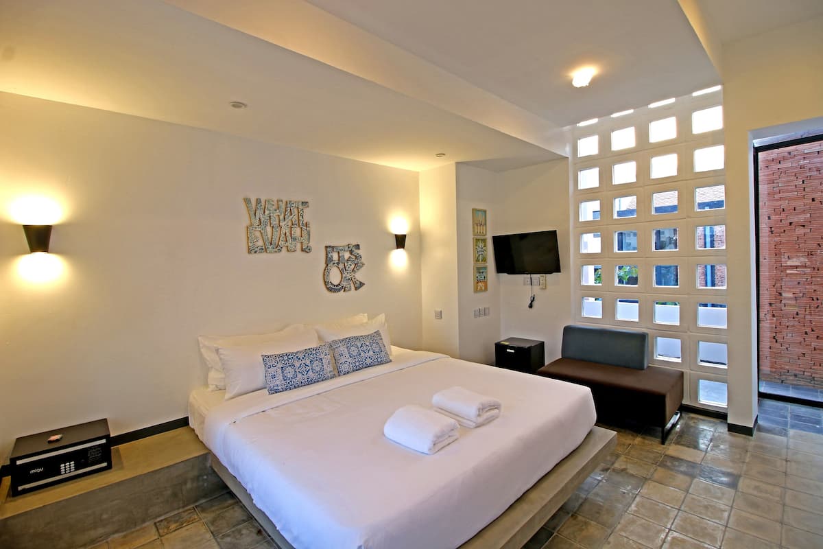 A hotel room with a large bed, a flat-screen TV, a seating area, and a view through a window with a brick wall.