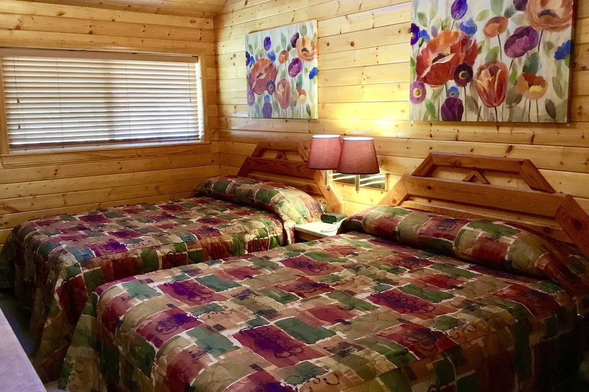 A cabin with two beds, wooden walls, and floral artwork.