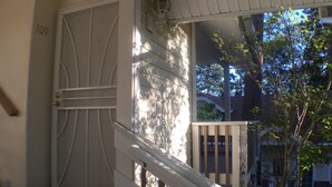 A white door with a number plate, a white railing, and a view of a tree and a building in the background. - Giant Oaks Lodge (Running Springs)