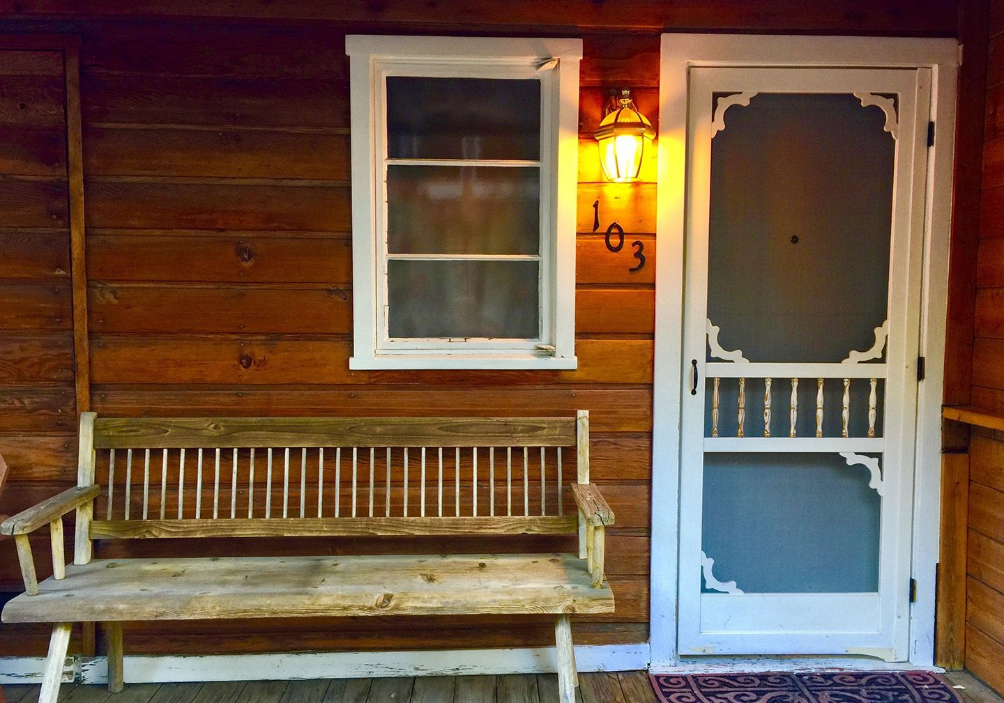 Una cabaña de madera con un banco, una ventana y una puerta con el número 103.