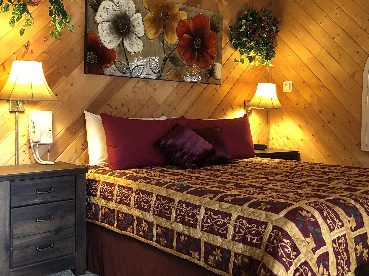 Une chambre à coucher avec un plafond en bois, un lit recouvert d’une couvre-lit à motifs, deux lampes de chevet, un téléphone et une œuvre d’art accrochée au mur.