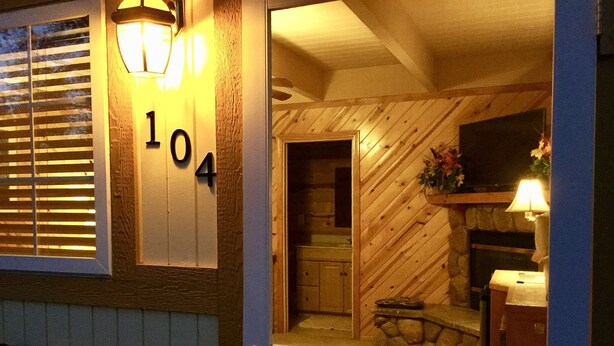 A wooden house with a number '104' on the door, a stone fireplace, and a wooden interior. - Giant Oaks Lodge (Running Springs)
