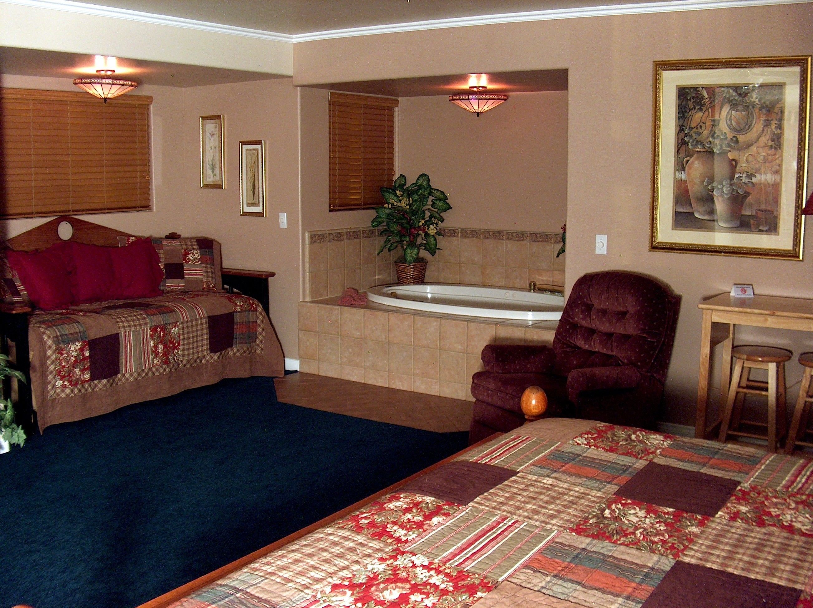 Een hotelkamer met een bed, een stoel, een bureau, een badkuip en een schilderij aan de muur.