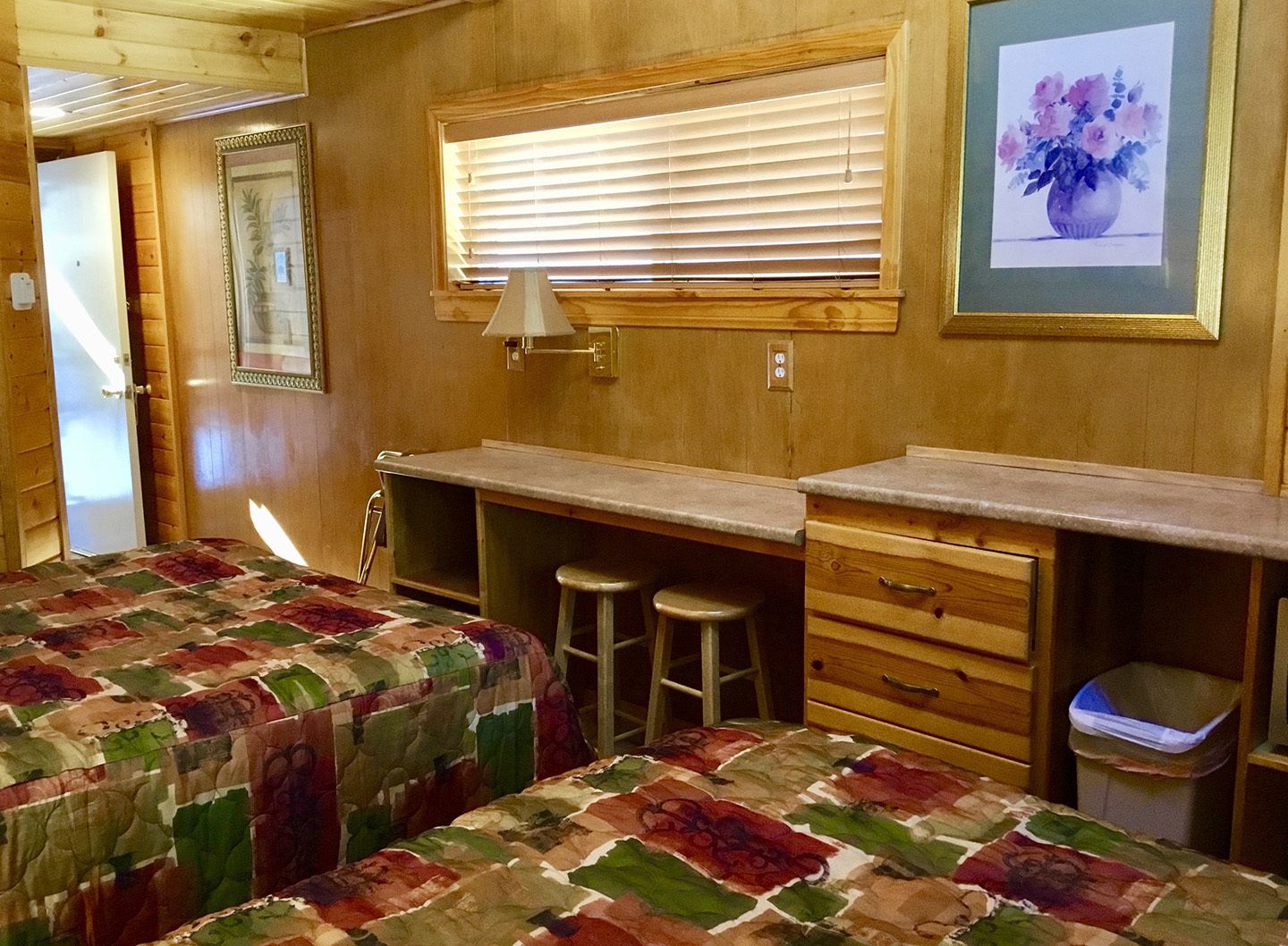 A cozy cabin bedroom with two beds, a desk, and a window with blinds.