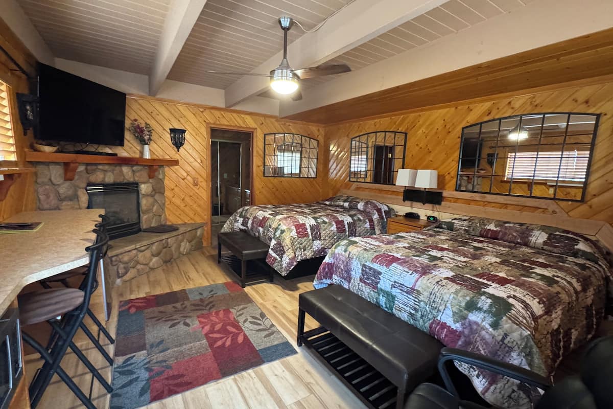 A cozy cabin with a stone fireplace, a large bed with a quilt, a dining area with a table and chairs, and a television mounted on the wall.