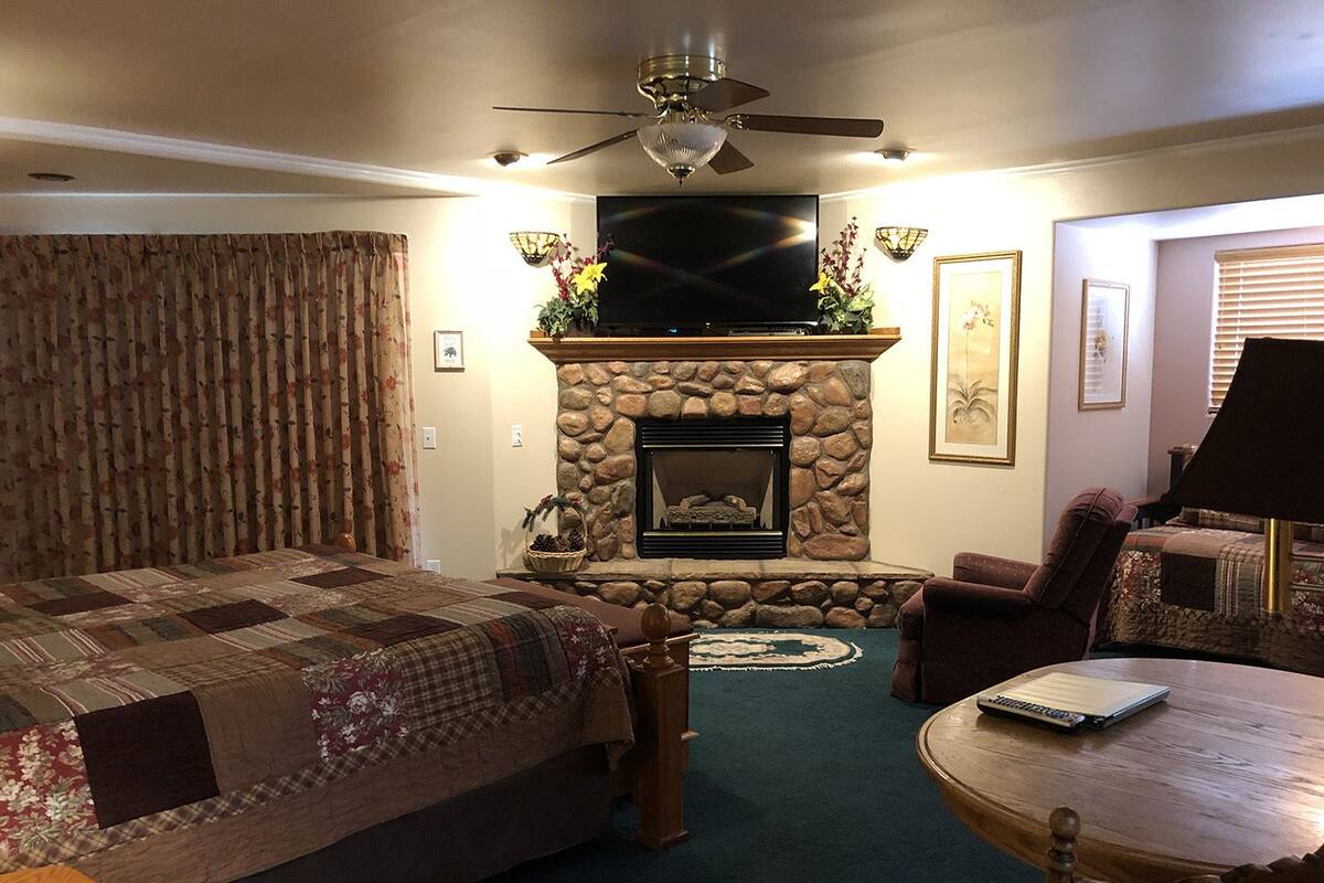 A cozy living room with a stone fireplace, a television mounted above it, a comfortable sofa, a round wooden coffee table, and a ceiling fan.