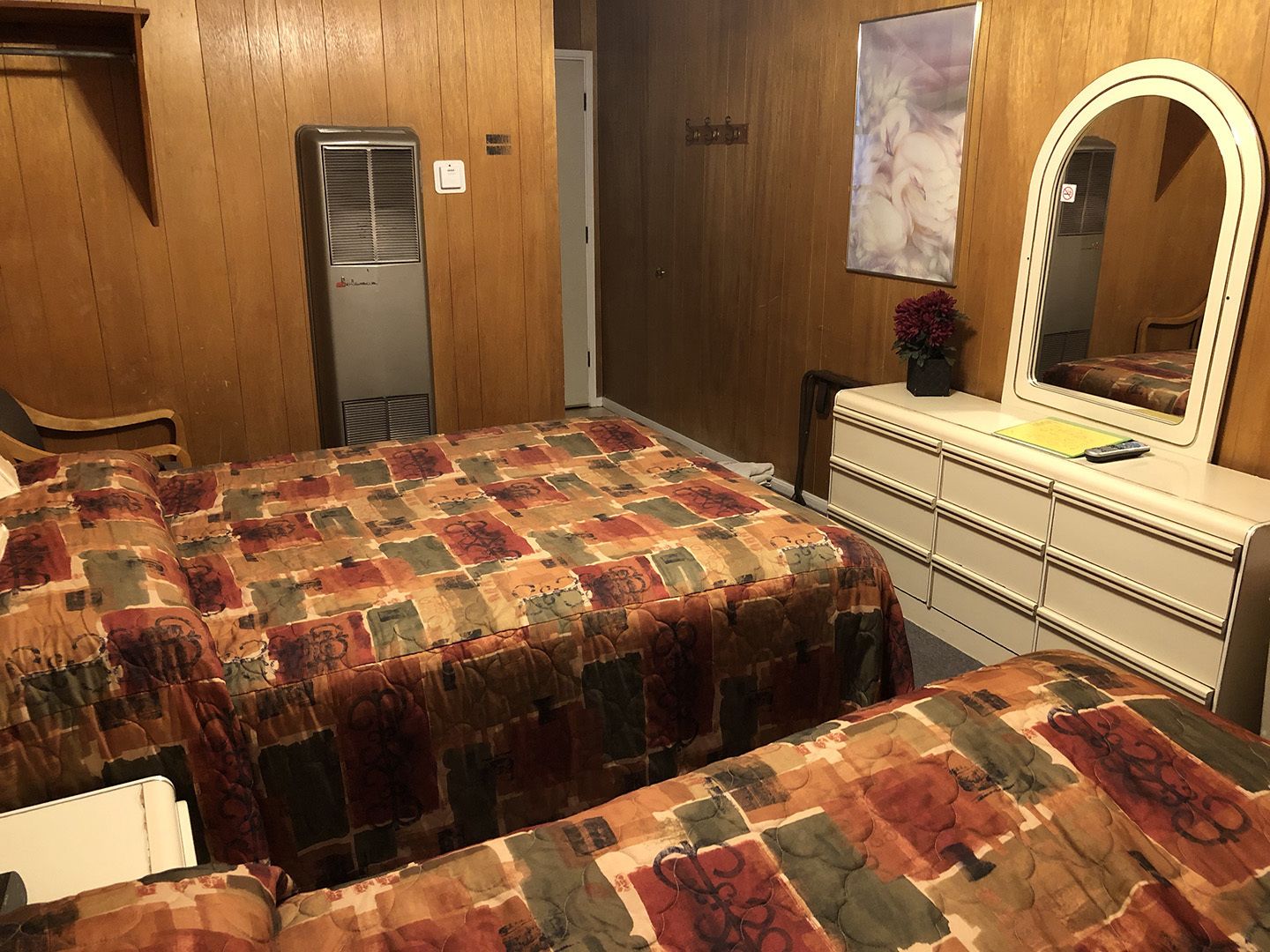 Une chambre avec deux lits, une commode, un miroir et un radiateur.