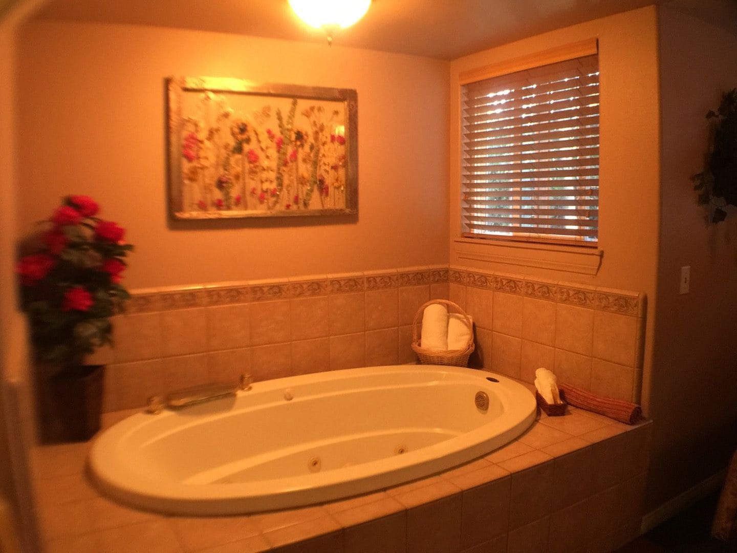 Ein Badezimmer mit einer freistehenden Badewanne, einem Fenster mit Jalousien, einem gerahmten Blumenbild und einem Blumentopf.