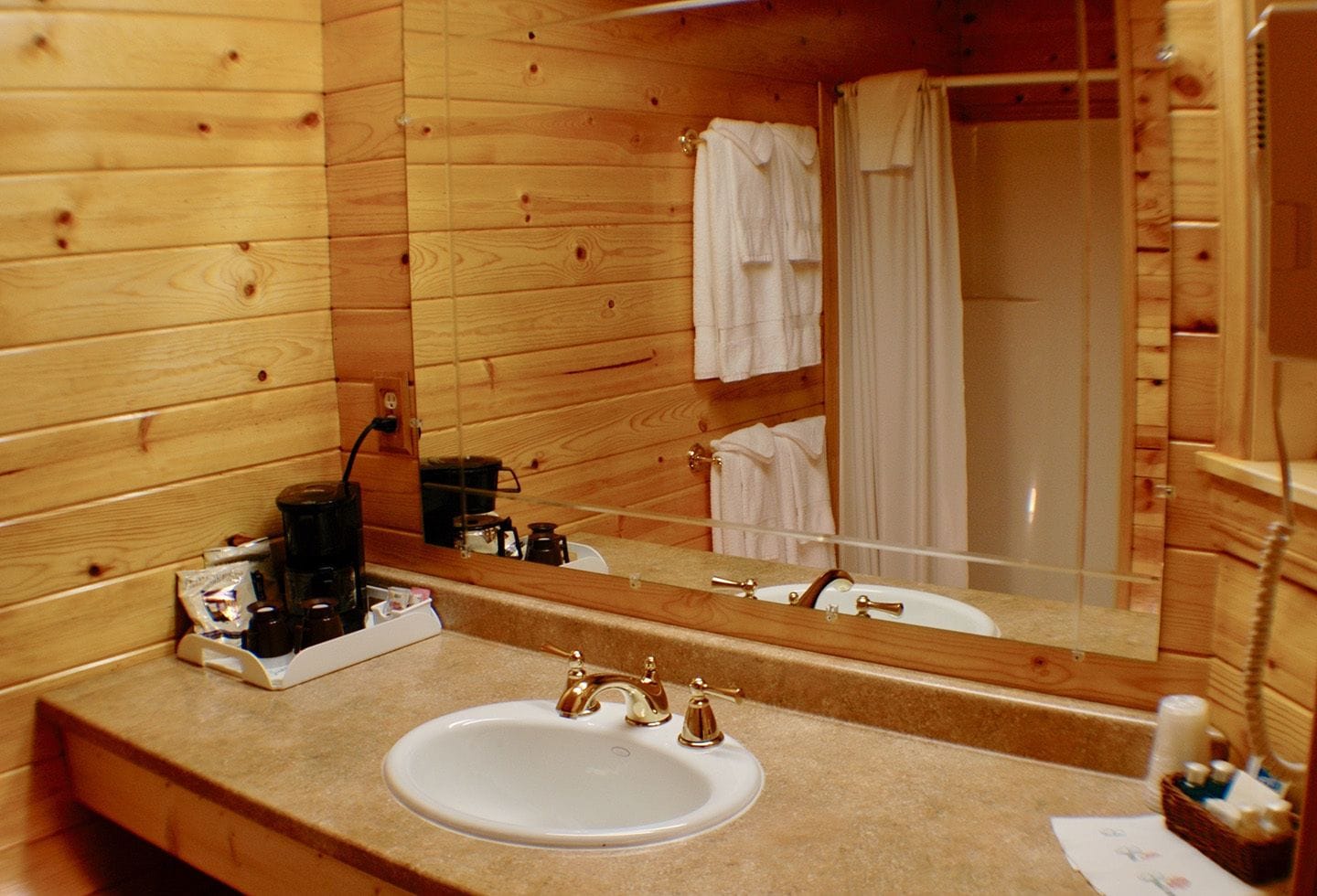 A wooden cabin bathroom with a sink, mirror, and shower.