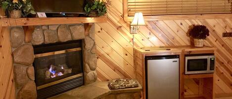 Ein gemütliches Blockhaus-Interieur mit Kamin aus Stein, Fernseher, Mikrowelle und kleinem Kühlschrank.
