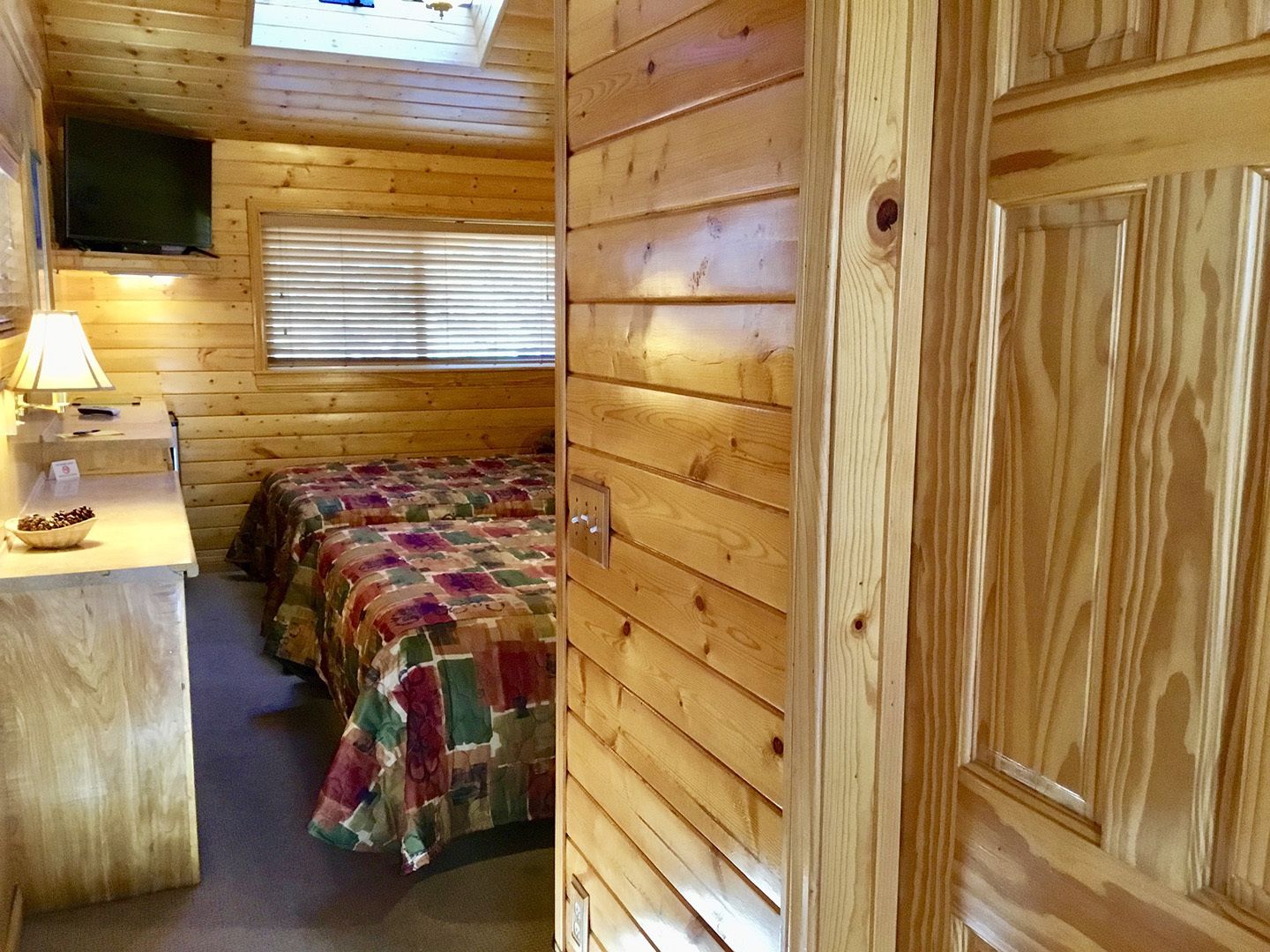 Una camera accogliente in una baita, con un letto, una scrivania con una lampada e una TV fissata al muro.
