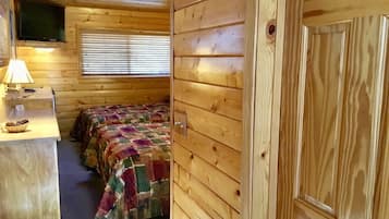 Una camera accogliente in una baita, con un letto, una scrivania con una lampada e una TV fissata al muro.