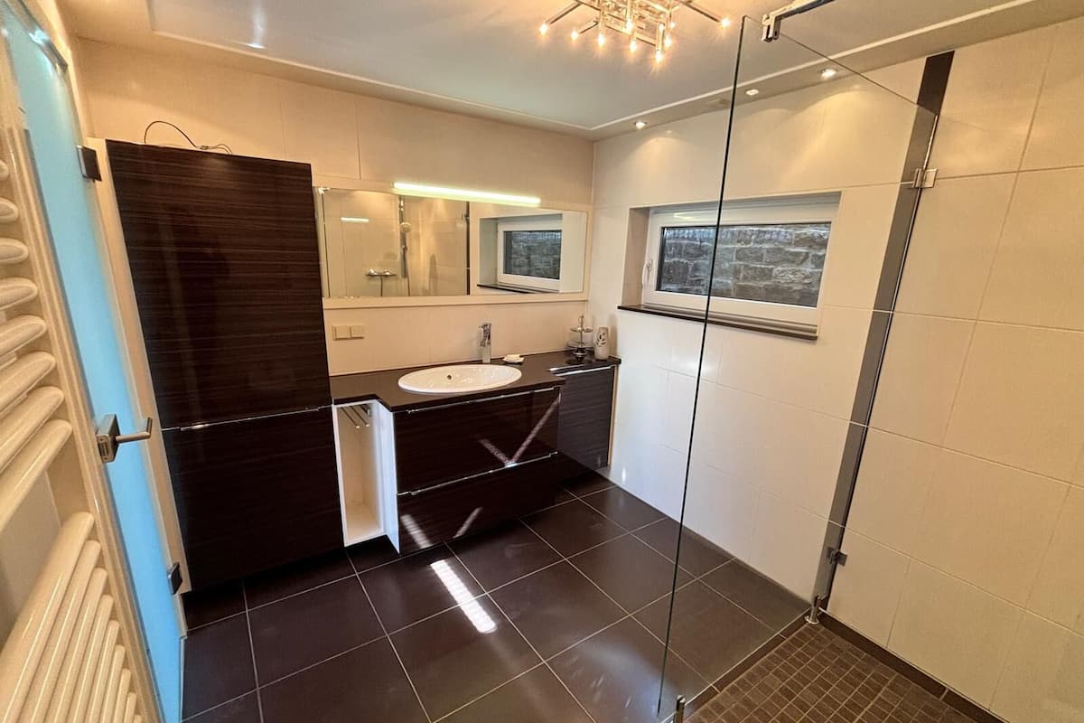 A modern bathroom with a glass shower enclosure, a large mirror, and a window.