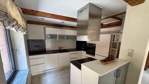 A modern kitchen with white cabinetry, a stainless steel range hood, and a built-in oven. - Landgasthof Kleine Kommode (Walkenried)