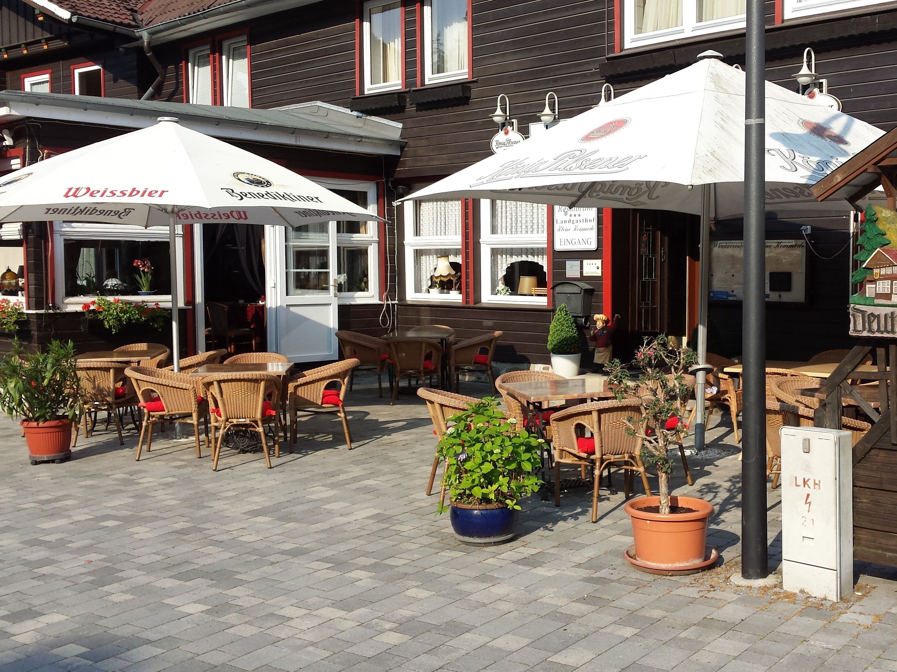 An outdoor seating area with wicker tables and chairs, potted plants, and umbrellas with Weissbier branding.