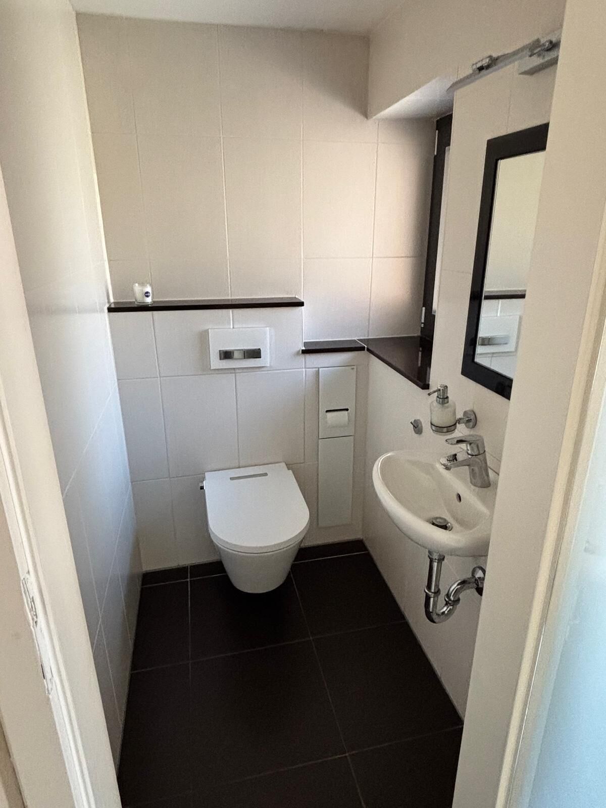 A small bathroom with a toilet, a sink, and a mirror.