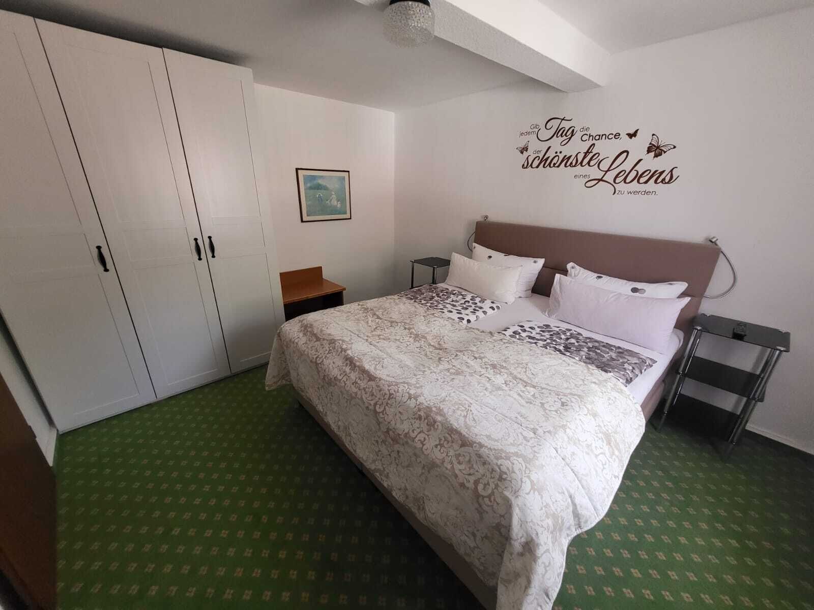 A bedroom with a large bed, a wardrobe, a bedside table, and a wall decoration.