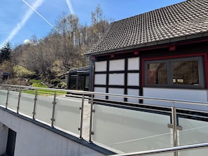 A building with a tiled roof, a balcony with metal railings, and a view of trees and a clear sky.