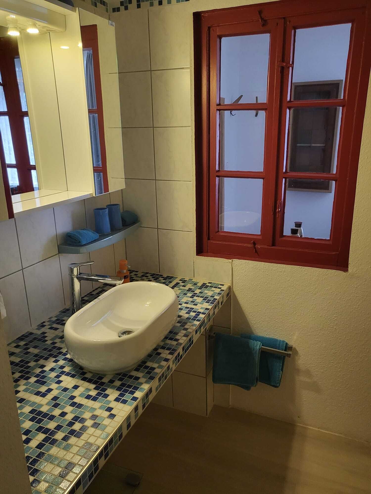 A bathroom with a white sink, a mirror, and a window with a red frame.