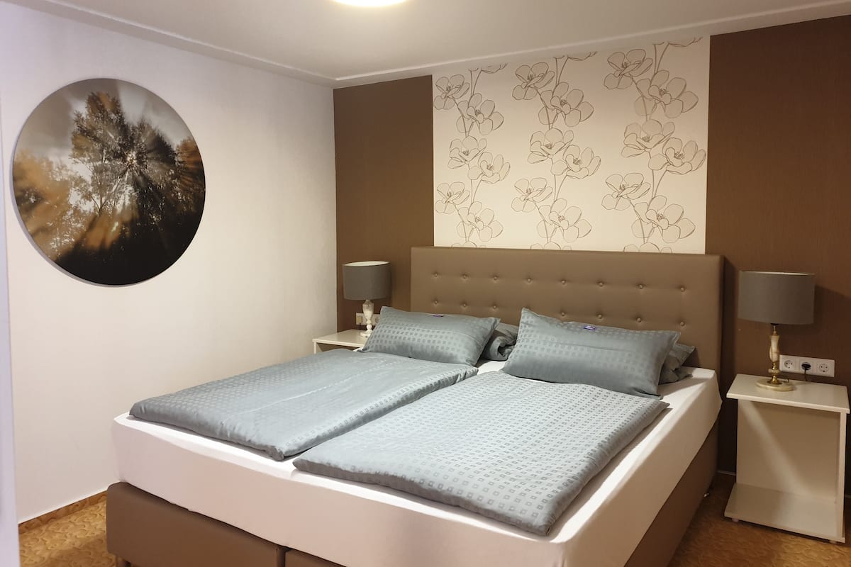 A double bed with a headboard, two bedside tables with lamps, a wall-mounted round mirror, and a floral-patterned wall.