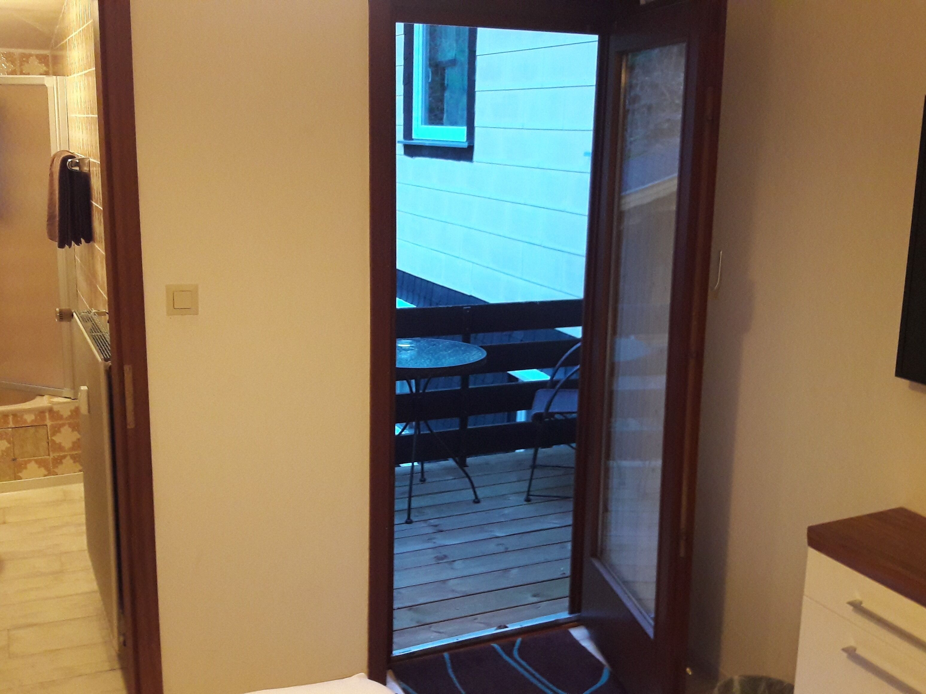 Een smalle deuropening die uitkomt op een houten terras met een tafel en stoelen.