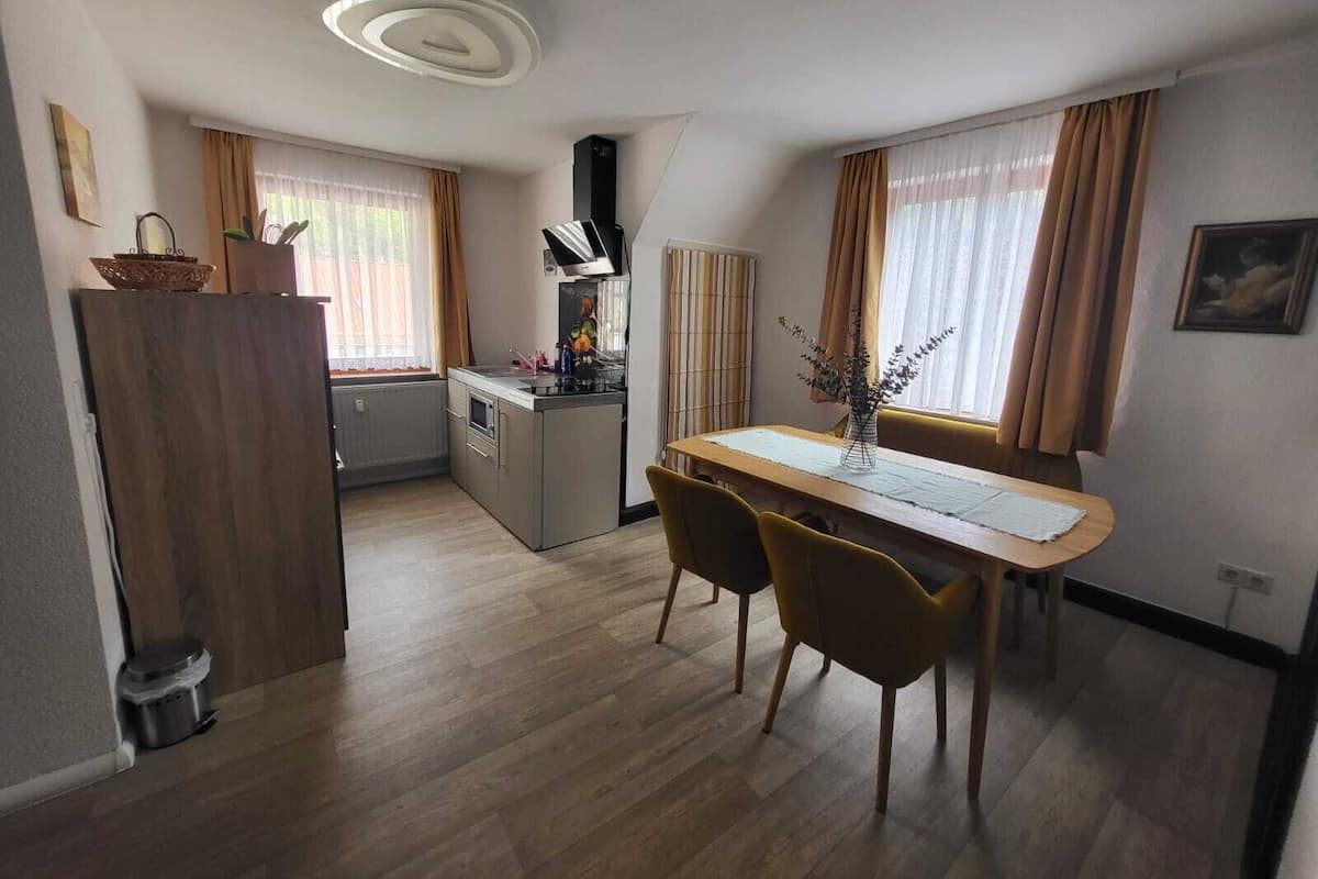 A compact kitchen with a dining area, wooden flooring, and a modern ceiling light fixture.