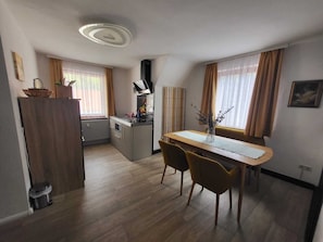 A compact kitchen with a dining area, wooden flooring, and a modern ceiling light fixture.
