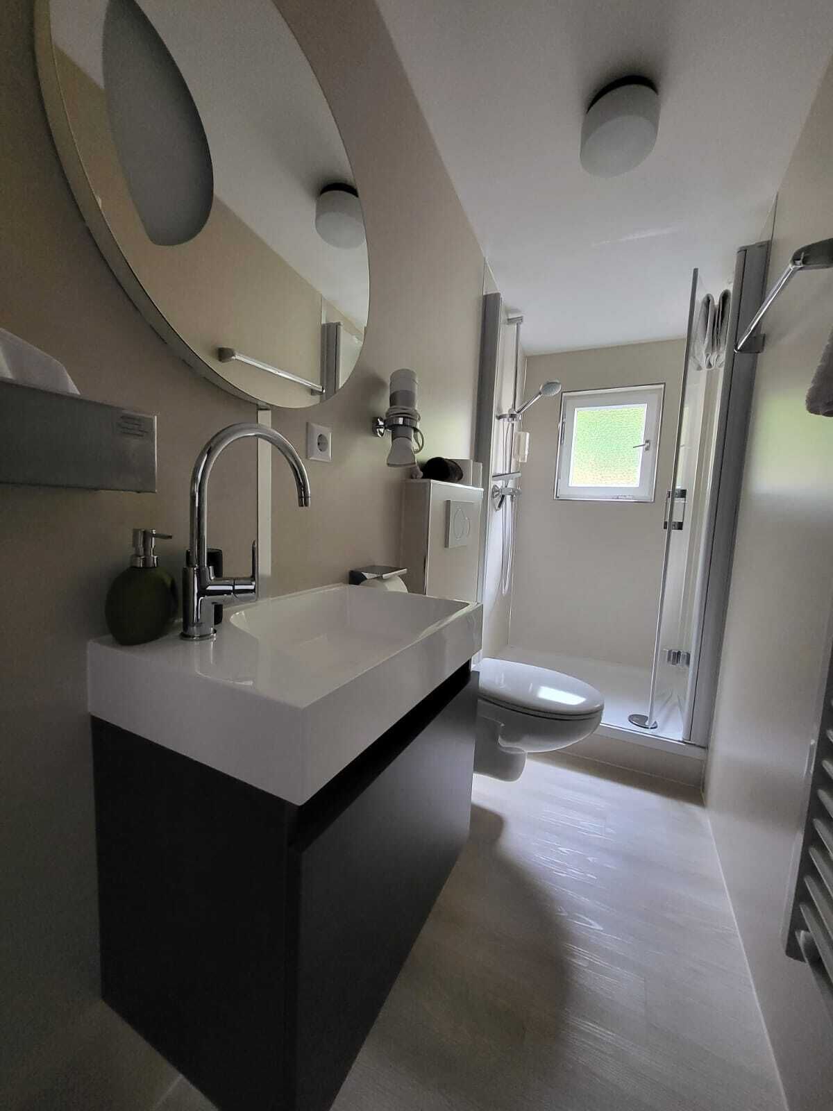 Et moderne badeværelse med en stor vask, spejl og bruseniche.