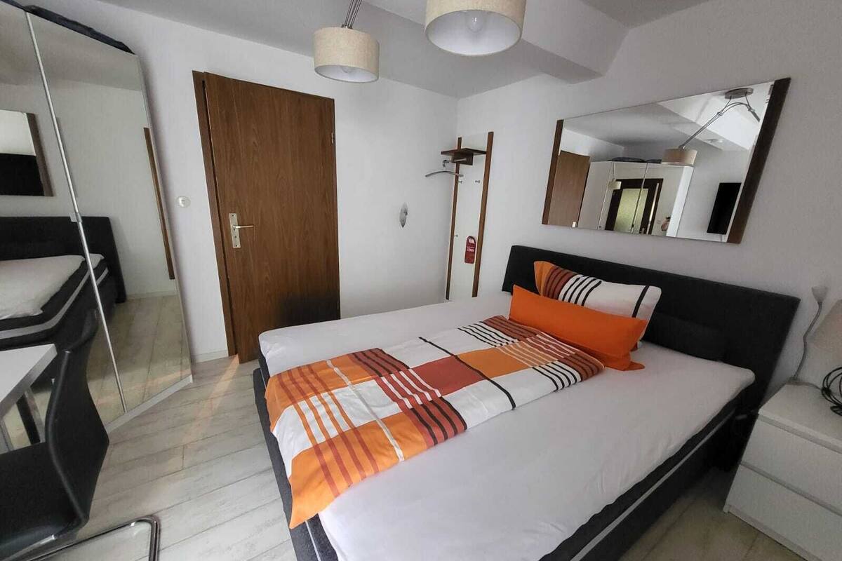 A modern hotel room with a large bed, a wooden door, a mirror, and a small desk.