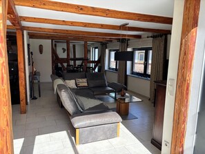 A modern living room with a sofa, a glass coffee table, and wooden beams on the ceiling. - Landgasthof Kleine Kommode (Walkenried)