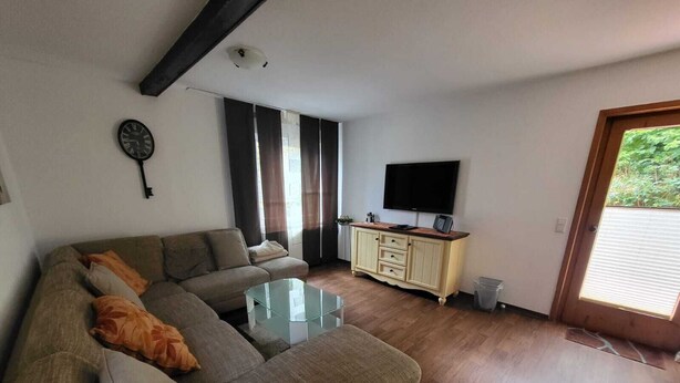 Una sala de estar con un sofá, una mesa de centro de vidrio, un televisor sobre un mueble y una puerta que da al exterior.