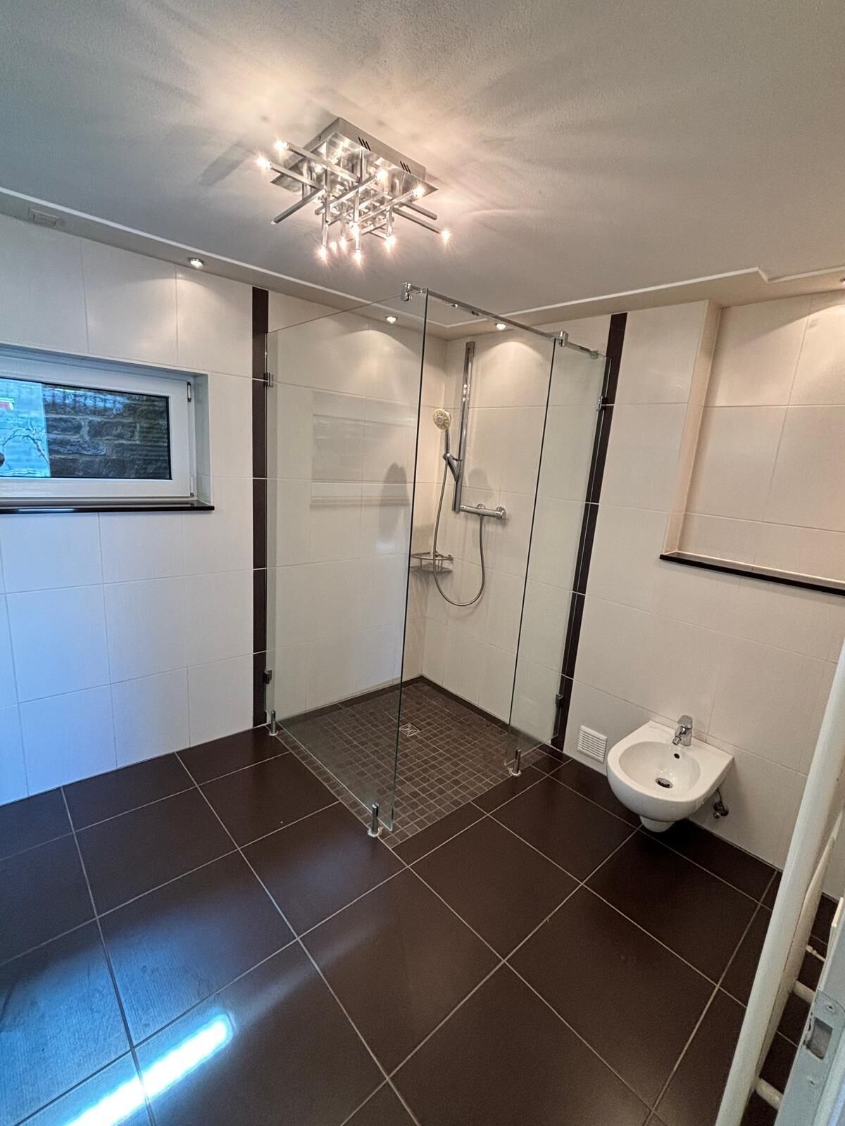 A modern bathroom with a glass shower enclosure, a bidet, and a window with a view.