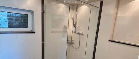 A modern bathroom with a glass shower enclosure, a bidet, and a window with a view.